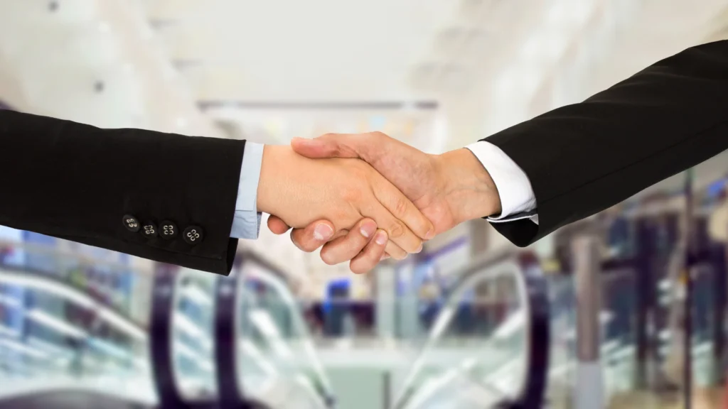 Deux personnes en costumes qui se serrent la main,  illustrant le métier d'apporteur d'affaire en assurance.