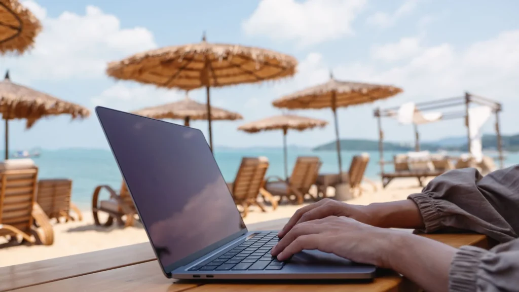 une personne travaillant sur un ordinateur portable dans un cadre détendu sur la plage, illustrant la liberté pour devenir apporteur d'affaires