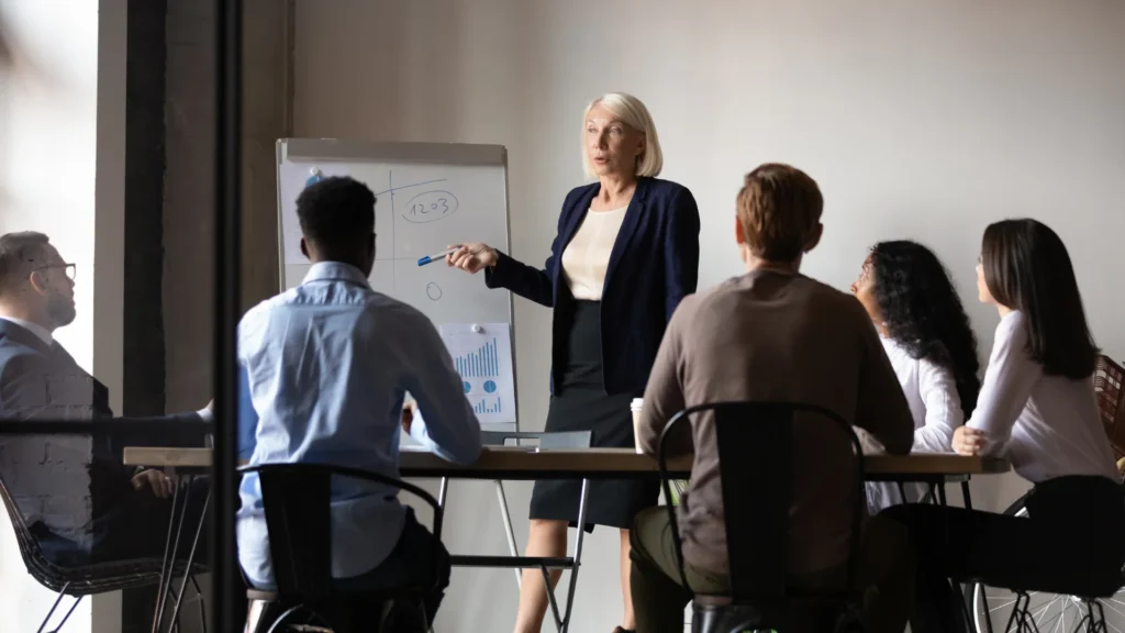 Formation en salle : une formatrice donne une présentation à un groupe de professionnels, illustrant les compétences en négociation et relationnel nécessaires pour devenir apporteur d'affaires